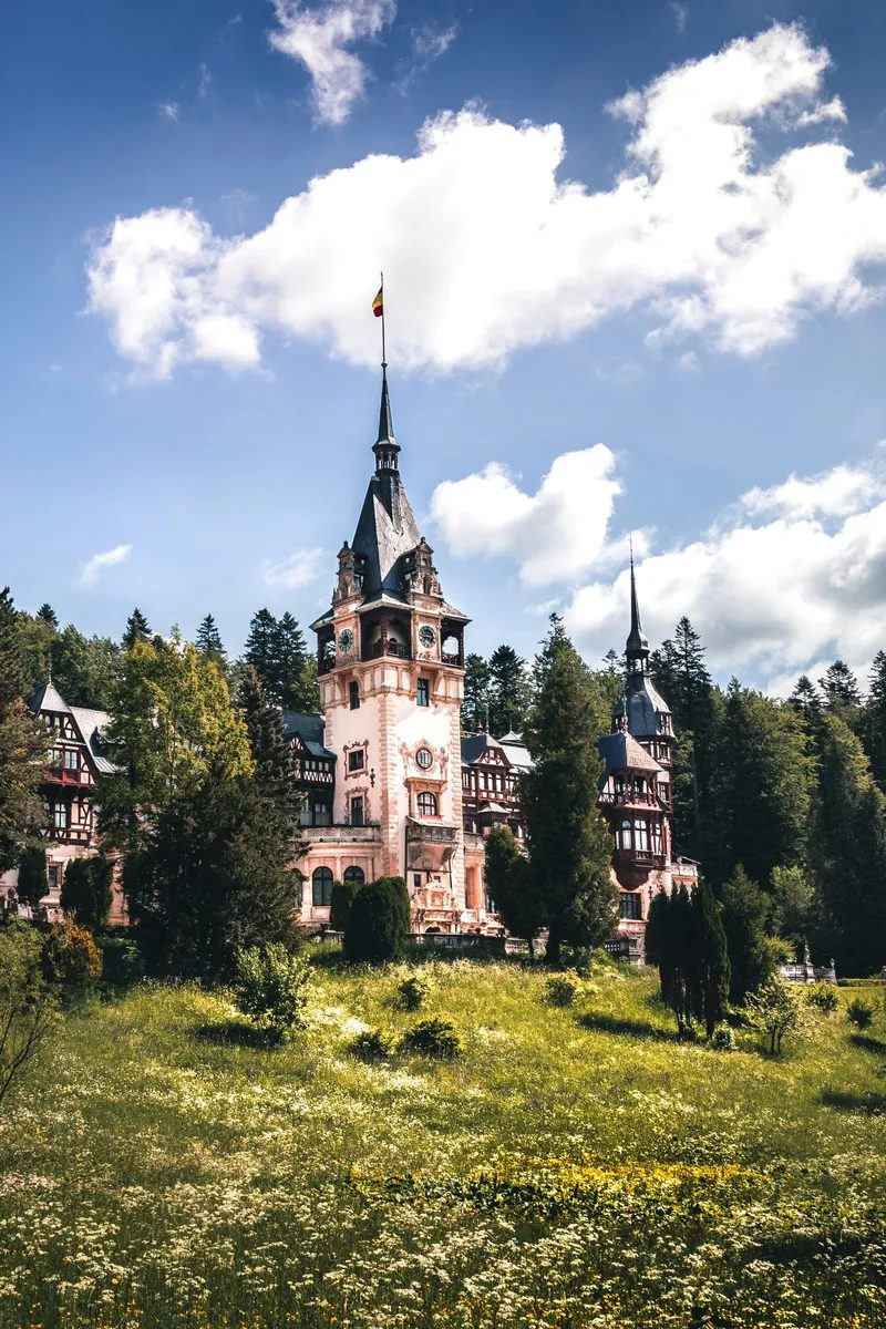 Peleș Castle with its tall spires and timber-framed façade against the wooded Carpathian mountainside above Sinaia